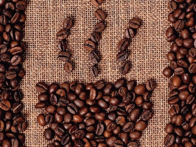 Fototapeta kubek z parą z ziaren kawy na tle z juty