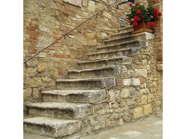 Fototapeta przedstawiająca stare kamienne schody z ceglaną ścianą i kwiatami