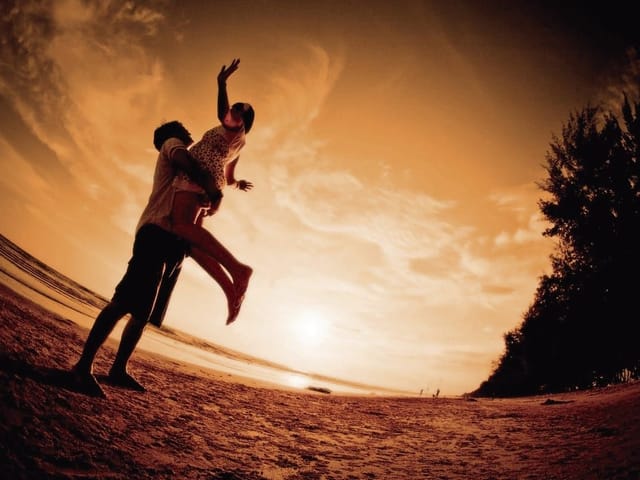 Fototapeta przedstawiająca parę na plaży o zachodzie słońca z drzewami i chmurami