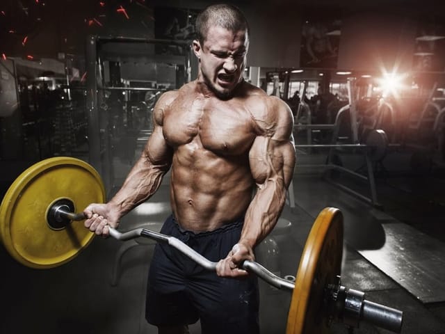 Fototapeta przedstawiająca umięśnionego mężczyznę podnoszącego sztangę z żółtą tarczą na siłowni