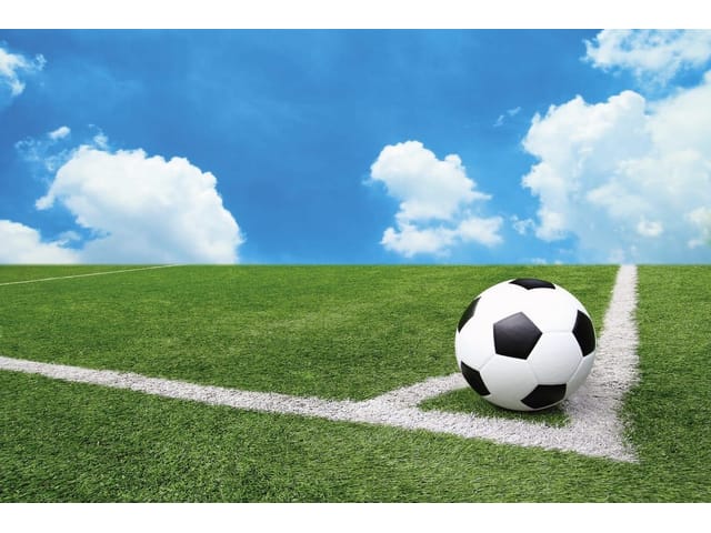 Fototapeta z piłką nożną na zielonym boisku, niebieskie niebo i chmury