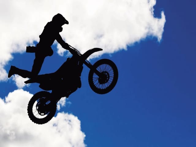 Fototapeta z motocyklistą na motorze w powietrzu na tle jasnego nieba