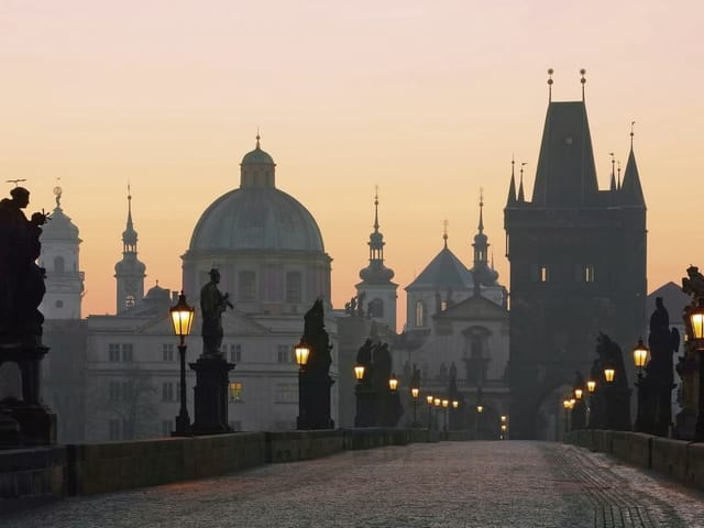 Fototapeta przedstawiająca most z kamiennymi rzeźbami i latarniami na tle miasta