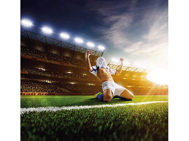 Fototapeta z piłkarzem na kolanach, stadionem i zachodem słońca
