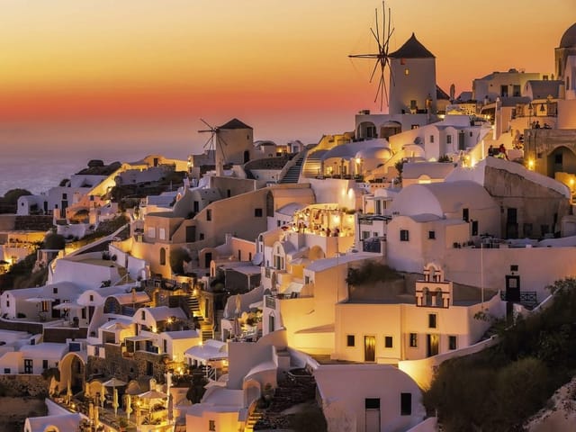 Fototapeta z białymi budynkami i wiatrakiem na wzgórzu o zachodzie słońca