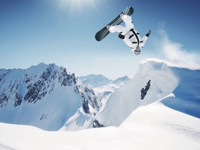 Fototapeta z snowboardzistą skaczącym nad śnieżnym stokiem w górach