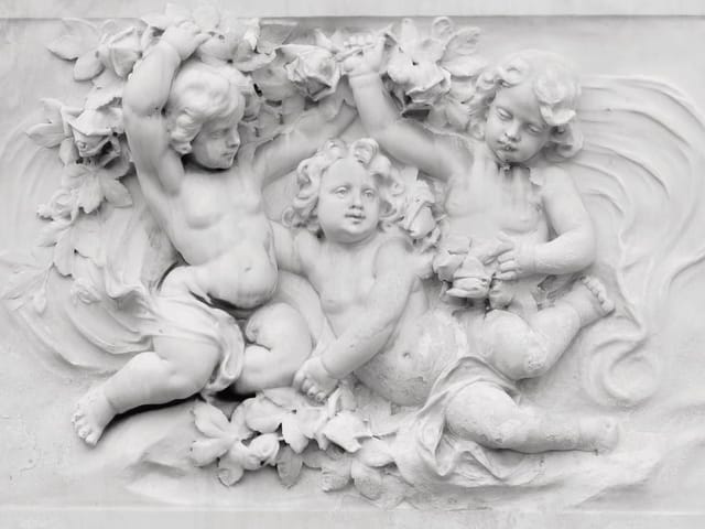 Fototapeta z trzema aniołkami w płaskorzeźbie, otoczonymi kwiatami