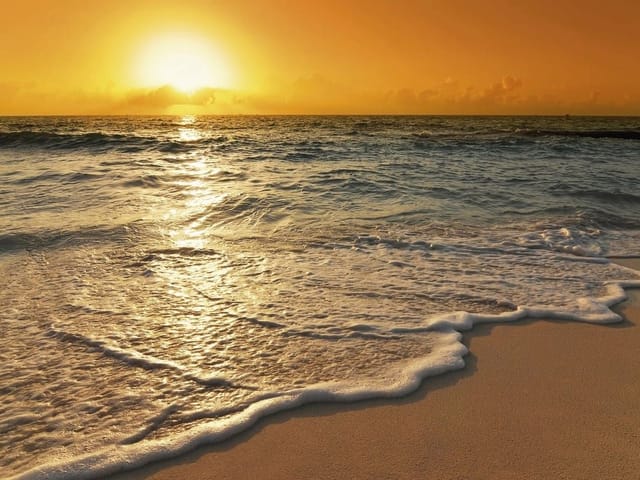 Fototapeta Zachód Słońca nad Oceanem (mpn: 2115) Fototapeta przedstawiająca zachód słońca nad oceanem z piaszczystą plażą i pomarańczowym niebem.