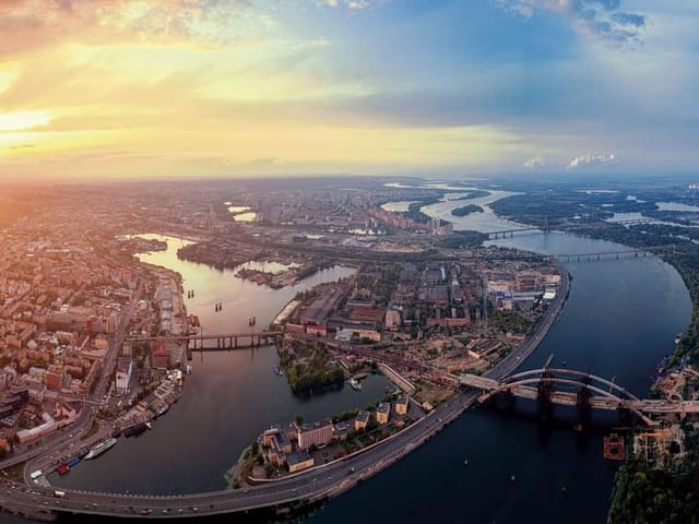 Fototapeta przedstawiająca panoramę miasta z szeroką rzeką i mostami o zachodzie słońca