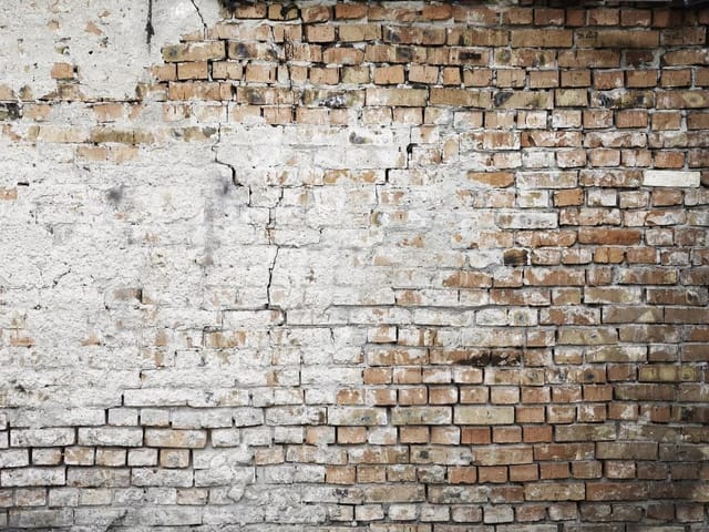 Fototapeta przedstawiająca starą ceglaną ścianę z widocznymi pęknięciami i nierówną powierzchnią