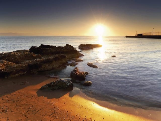 Fototapeta z zachodem słońca nad morzem, skały i piasek na plaży