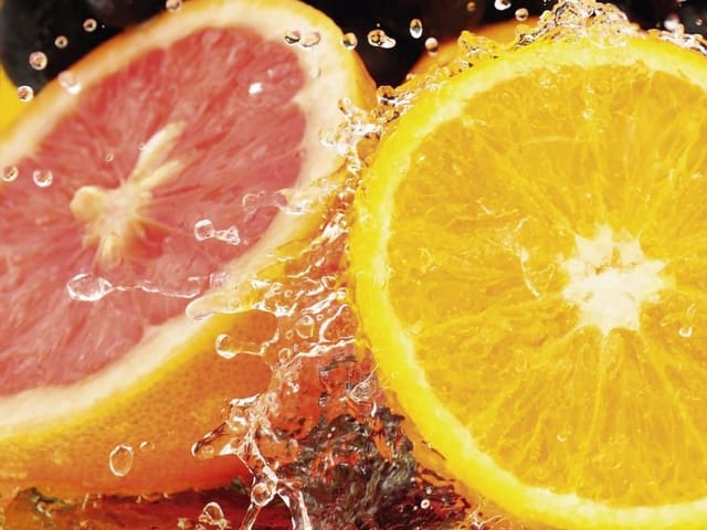 Fototapeta z plasterkami pomarańczy i grejpfruta w rozpryskującej się wodzie