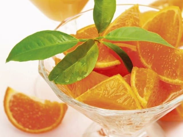 Fototapeta z kieliszkiem pełnym pomarańczy i zielonymi liśćmi na jasnym tle