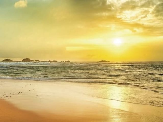 Fototapeta przedstawiająca plażę z złotym piaskiem i spokojnymi falami oceanu o zachodzie słońca.
