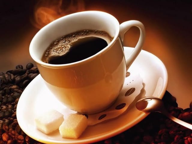 Fototapeta z filiżanką gorącej kawy na spodku i ziarnami