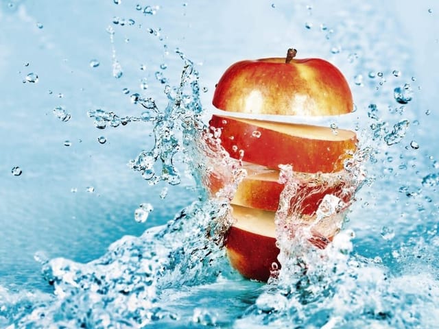 Fototapeta z jabłkiem pokrojonym w plastry i rozpryskami wody na jasnoniebieskim tle