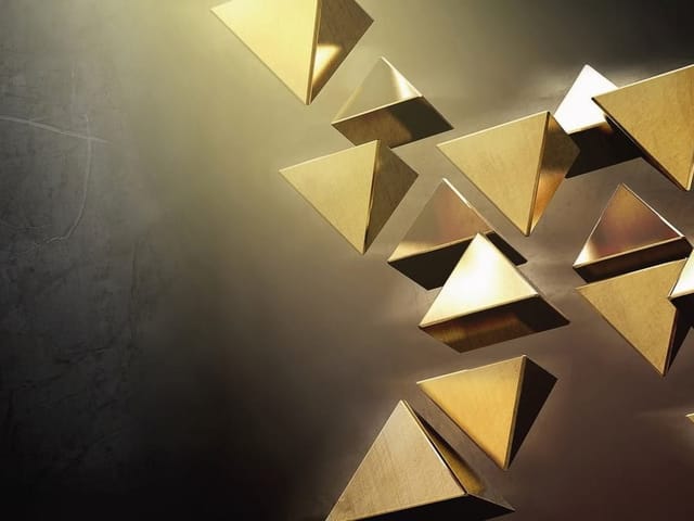 Fototapeta przedstawiająca złote trójkątne bryły na ciemnym tle z cieniami