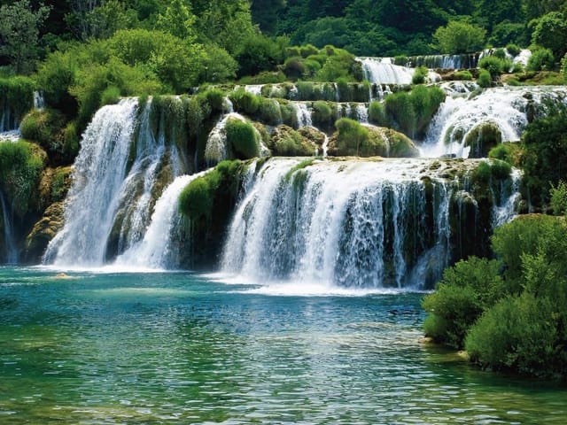 Fototapeta z wodospadem w otoczeniu zieleni i przejrzystą wodą