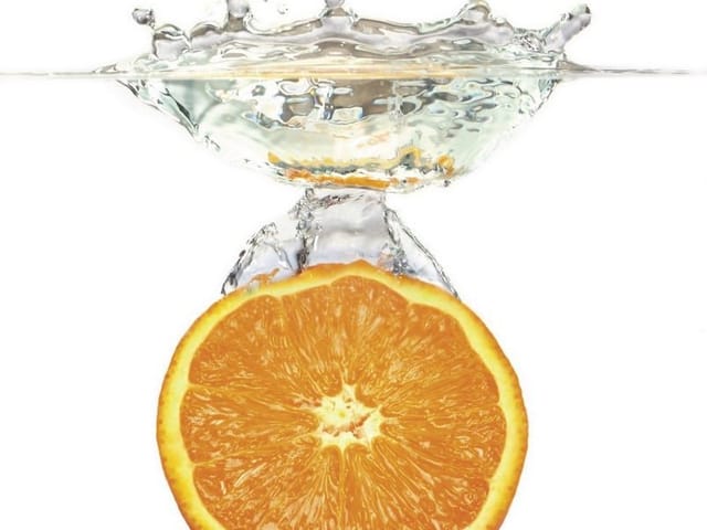 Fototapeta z plasterkiem pomarańczy w wodzie na białym tle, dynamiczny rozprysk