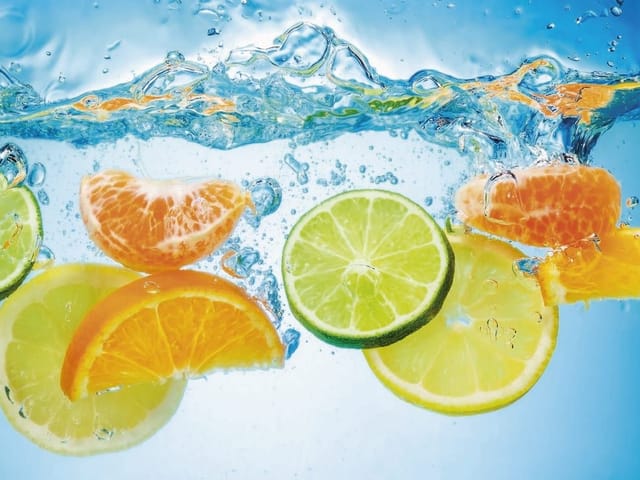 Fototapeta z plastrami limonki i pomarańczy w wodzie pełnej bąbelków