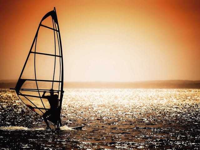 Fototapeta Windsurfer o zachodzie słońca (mpn: 910) Fototapeta z windsurferem na wodzie przy zachodzącym słońcu i pomarańczowym niebie