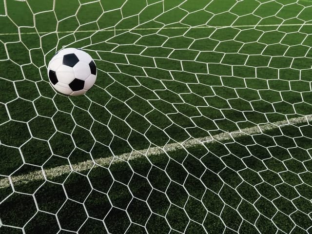 Fototapeta z piłką nożną uderzającą w siatkę na zielonej murawie